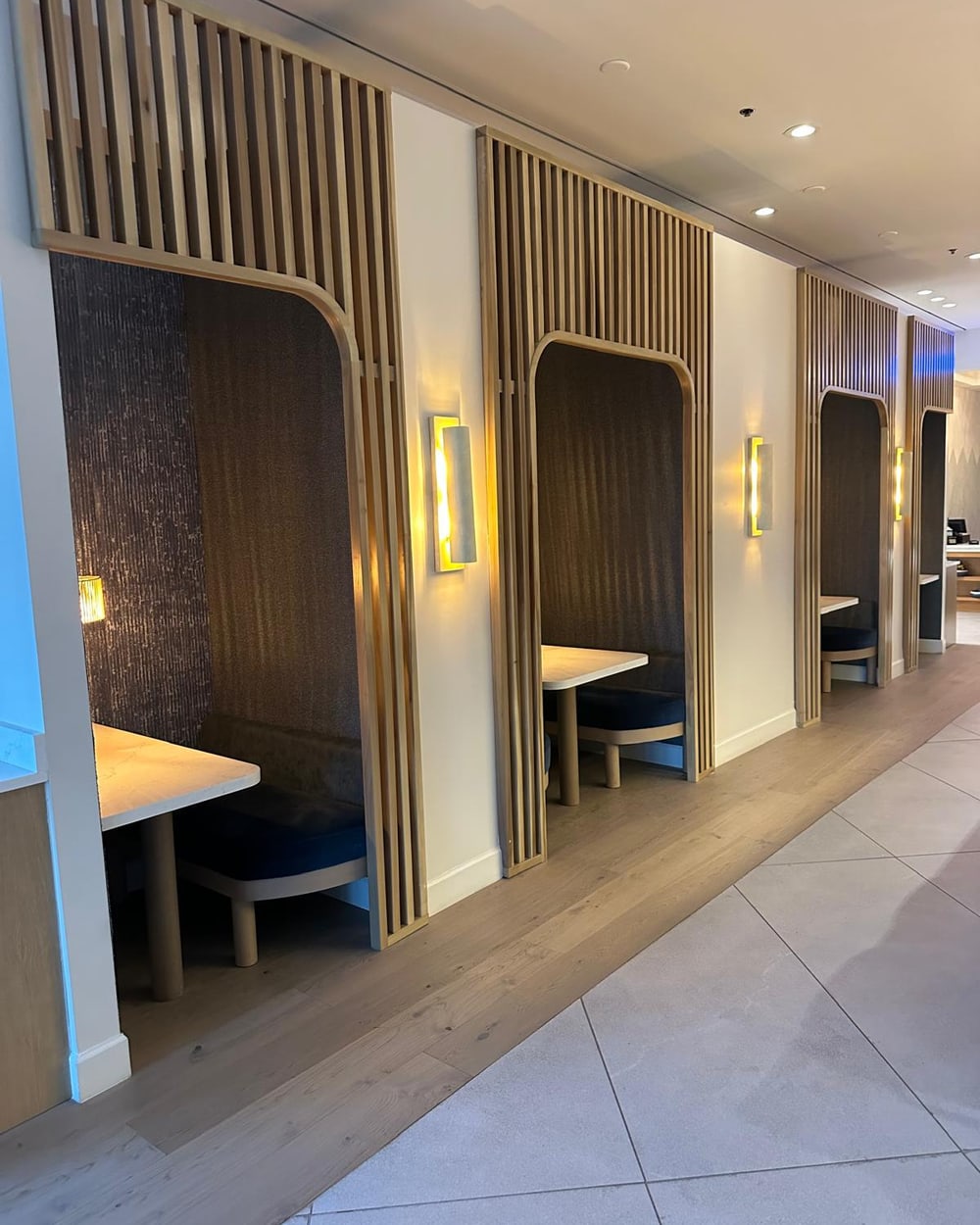 A run of custom private dining booths with oak slat screens, upholstered backs and stone tops