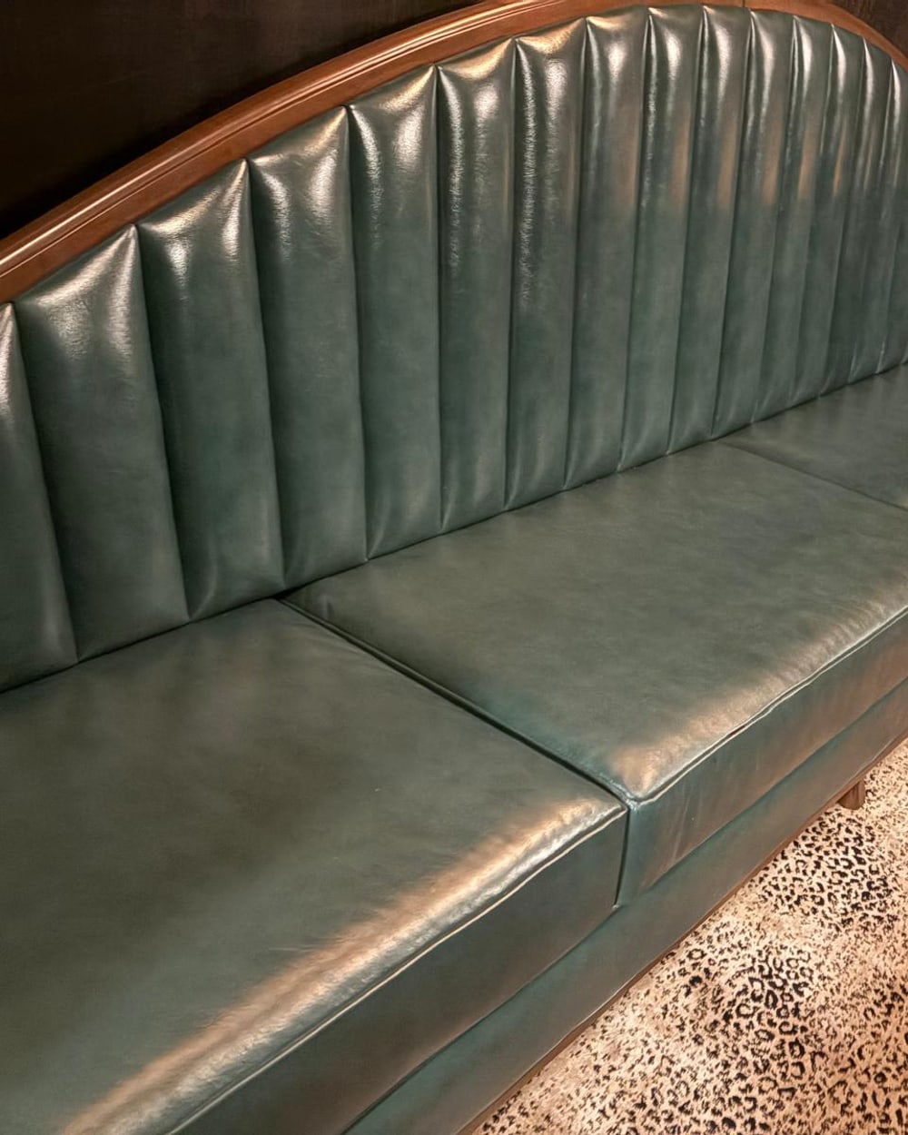 Channel-tufted green leather banquette with a hand-carved wood crest rail following the curve of the back
