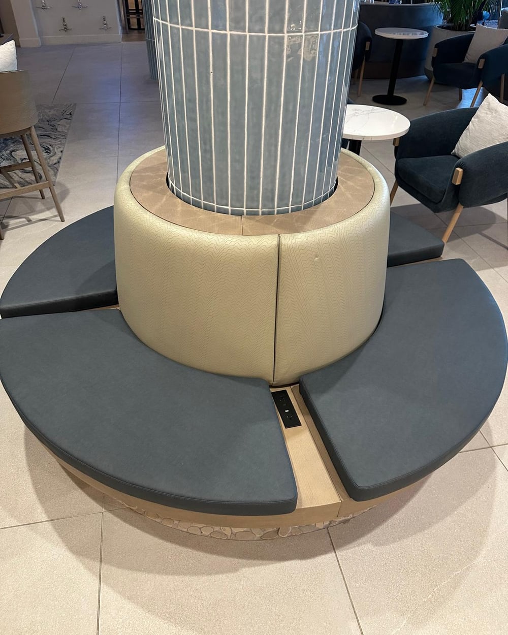Custom round upholstered bench built to wrap a structural column, with power outlets set into the base